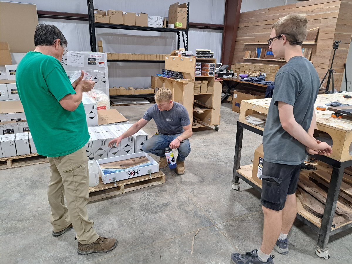 Man kneeling down over an epoxy ocean serving tray, explaining the process to two people standing up and looking down at him