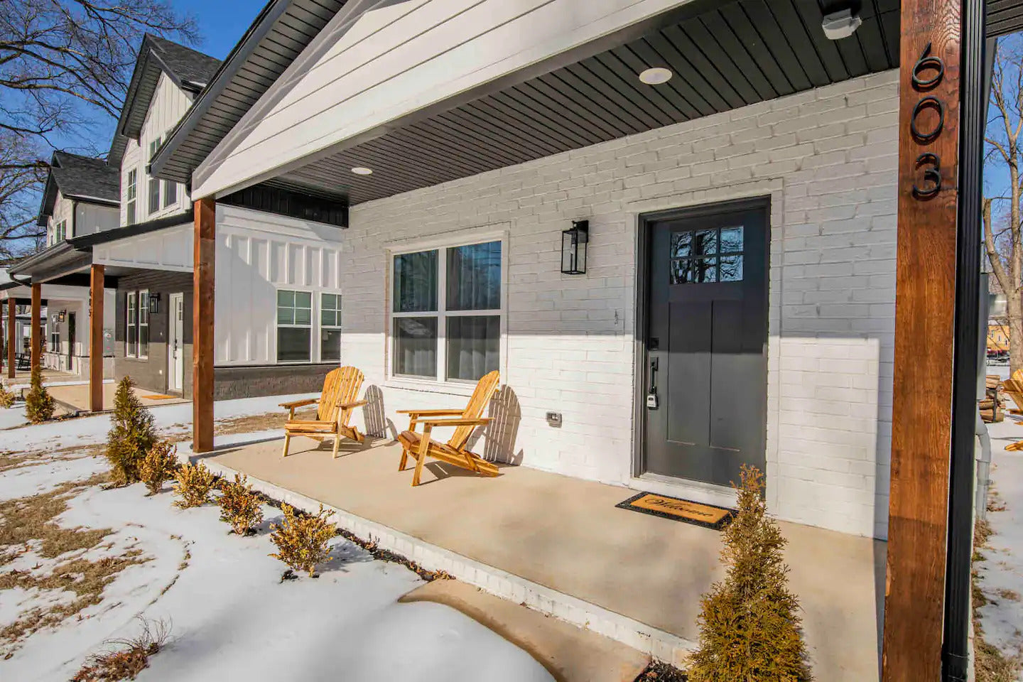 Picture of a white brick house with a front porch, with two chairs sitting on the porch.