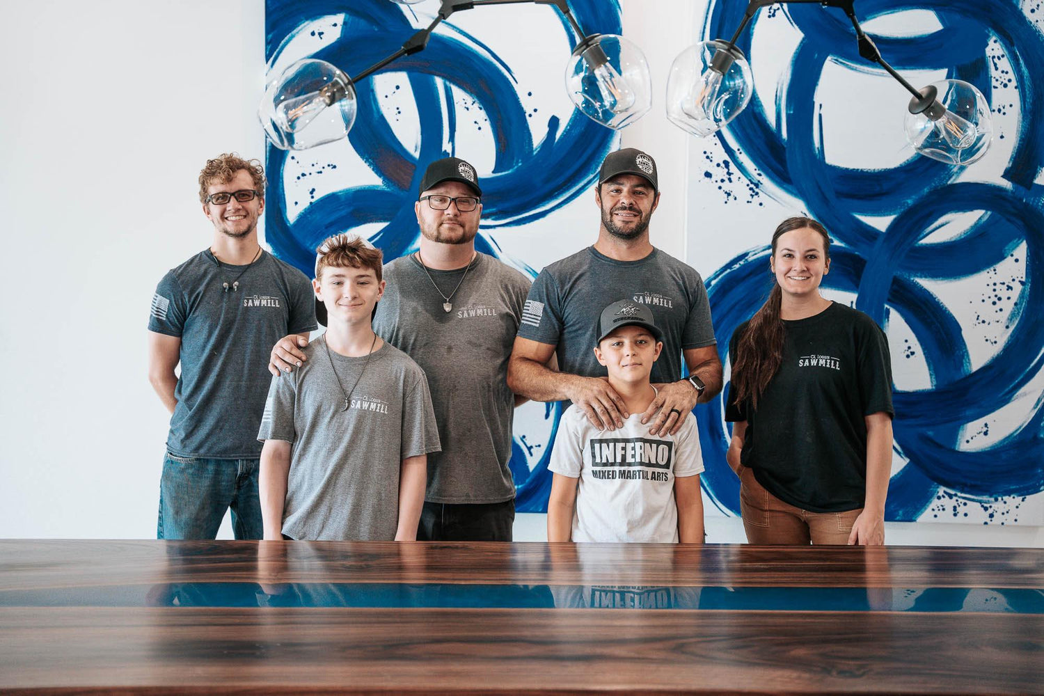 Six people standing in front of a blue epoxy river table. Blue circles are painted on the wall behind them in an artistic looking way.